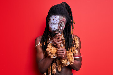 african native guy trying to use modern cutlery, holding spoon and fork in hands, isolated over red background