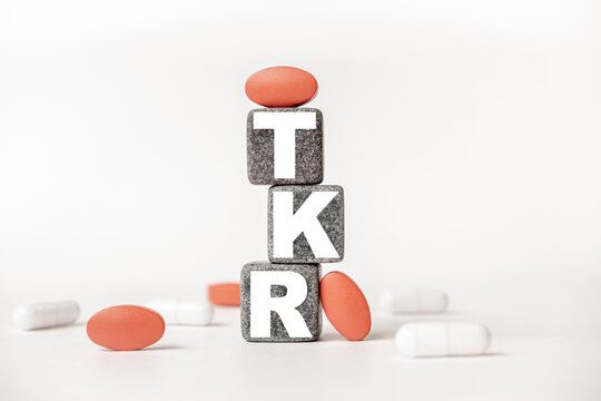 a group of white and red pills and cubes with the word TKR Total knee replacement on them, white background. Concept carehealth, treatment, therapy.