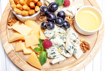 Board with different types of cheese. Cheeses mix set dor blu chedar parmesan brie honey sauce finger bread and grape on wooren palte. Restaurant menu breakfast plate. Healthy snack assortment.