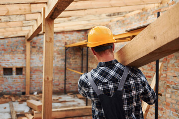 Transporting wooden boards. Construction worker in uniform and safety equipment have job on building