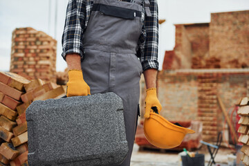 Hard hat and case in hands. Construction worker in uniform and safety equipment have job on building