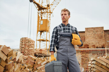 Hard hat and case in hands. Construction worker in uniform and safety equipment have job on building