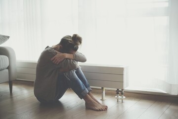 A lonely young woman feels depressed and stressed as she sits on the floor with her head in her...