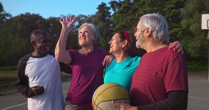 Group of seniors embracing and smiling holding basketball outdoors