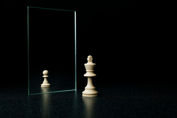 king is reflected in the mirror as a pawn on white background. underestimation of their abilities