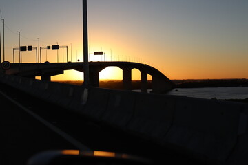 photo where the sunset behind a bridge through which a large river passes, in the late afternoon