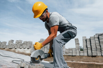 Slicing by circular saw. Male worker in yellow colored uniform have job with pavement