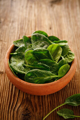 Fresh spinach  leaves in a ceramic bowl on a wooden background, close up view
