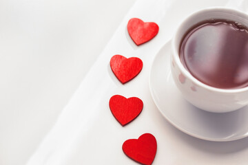 Top view red heart shaped figurins with white cup of tea on light background. Good morning with hot drink concept. Space for text. tonned