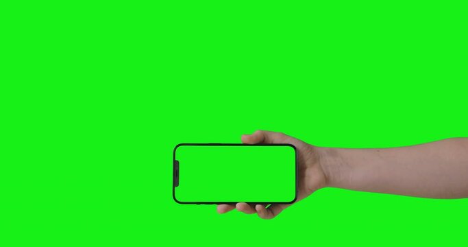 Woman hand holding the smartphone on green screen chroma key background. Mock-up for your product. The iPhone 12 Pro Max model in horizontal orientation landscape mode.