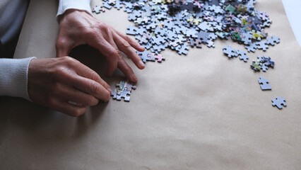 woman in white sweater doing puzzle.Female's hands and puzzle pieces on the table.