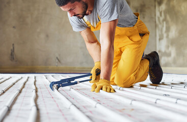 Many of pipes. Worker in yellow colored uniform installing underfloor heating system