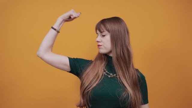 Angry and aggressive, shaking fist in a threatening way, domestic violence. Young attractive woman, dressed green shirt blonde hair, yellow background