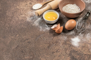 Baking utensils and ingredients. Eggs, flour, whisk and rolling pin on a rusty background. Baking...