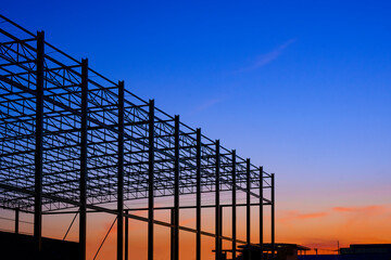 Silhouette low angle view of large industrial building structure in construction site area against colorful twilight sky background - Powered by Adobe
