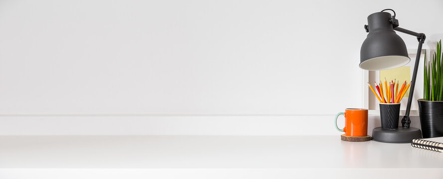 Desk at home office with supplies, lamp, pencils, brushes and blank frame mockup. Homeschool creative, business web banner.