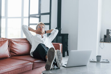 Fototapeta premium With laptop. Caucasian young guy in elegant white shirt indoors at home