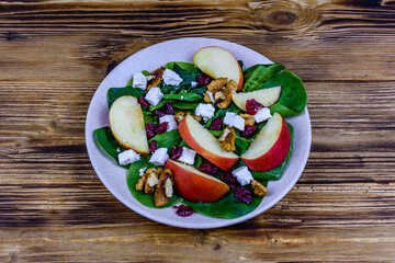 Salad with spinach leaves, feta cheese, cranberries, walnuts and apple in a ceramic plate