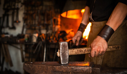 blacksmith performs the forging of hot glowing metal on the anvil