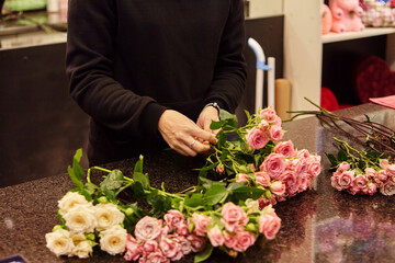 Florist works with colors. Flower seller chooses flowers for future bouquet. Flowers shop worker in a mask standing in flower shop and checking flowers in glass vase.