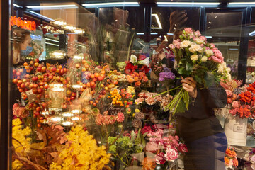 Florist takes flowers out of the fridge. Flower seller chooses flowers for future bouquet. Flowers shop worker in a mask standing in flower refrigerator and checking flowers in glass vase.