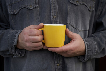 Man holding big yellow mug in his hands wearing grey jeans shirt. Slowing down concept. High quality photo