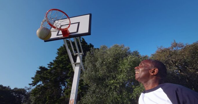 Senior african-american man dunking basketball on outdoors court