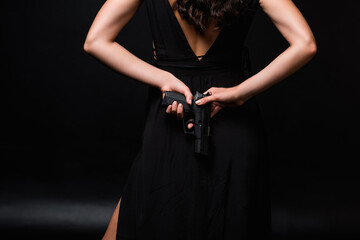 Fototapeta na wymiar cropped view of dangerous woman holding gun behind back on black