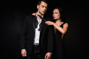 dangerous woman in dress holding knife near neck of man in suit isolated on black