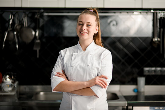 young beautiful smiling woman chef with arms crossed at kitchen