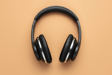 Close-up photo of stylish modern black chrome headphones over beige background.