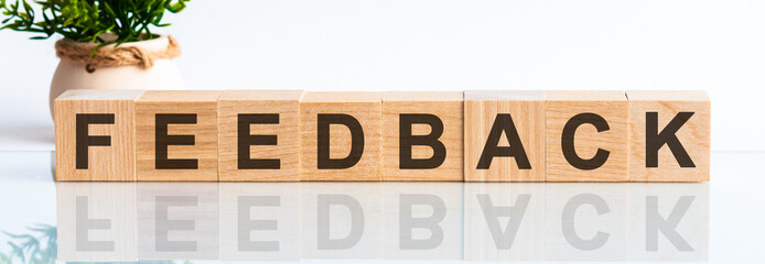 FEEDBACK motivation text on wooden blocks business concept white background. Front view concepts, flower in the background.