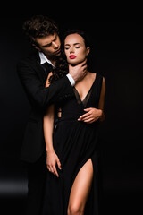 passionate man choking sexy and submissive woman in dress on black