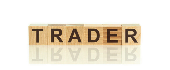 Wooden blocks with the text: trader. The text is written in black letters and is reflected in the mirror surface of the table.