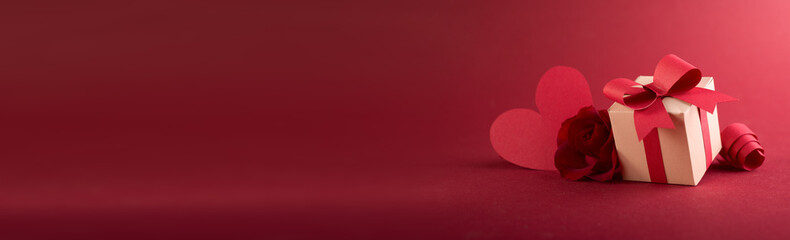 Paper art Valentine's day concept banner with hand made gift box, paper cut ribbon, bow, and a lot of hearts on a red background with space for text.