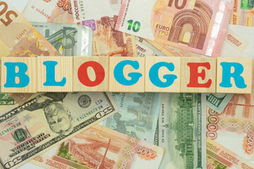The inscription blogger in multicolored cubes on the background of banknotes euro dollars rubles