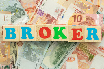 Obraz premium The inscription broker in multicolored cubes on the background of banknotes euro dollars rubles