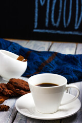 Still life in a coffee shop. White cup of coffee and chocolate chip cookies on a light wooden table. A cozy pastime.