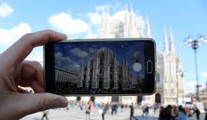Turista al Duomo di Milano in Primavera: cellulare, guglie e statue