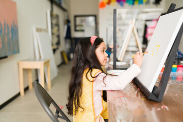 Profile of a latin elementary girl painting on a canvas during an art class