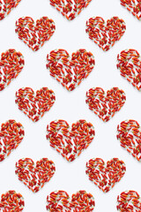 Spicy love concept with pattern from red hot chili peppers arranged into heart shapes of different sizes on a white background. Minimal modern idea.