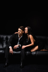young woman in dress seducing man in suit sitting on sofa on black