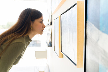 Hispanic woman studying closely a painting at the gallery