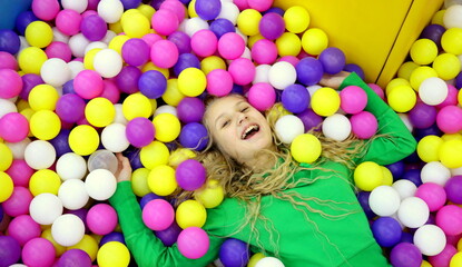 Fototapeta na wymiar A young blonde girl of European appearance with blond curly hair smiles at the children's playground and entertainment center.