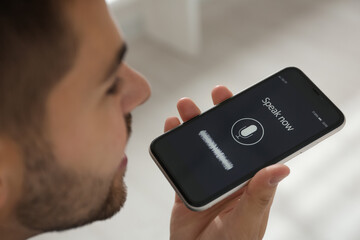 Young man using voice search on smartphone indoors, closeup
