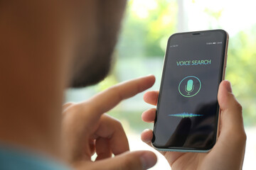 Young man using voice search on smartphone indoors, closeup