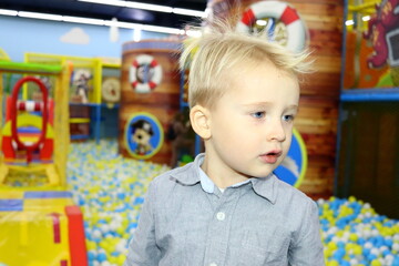 Fototapeta na wymiar A blond boy in a gray shirt plays in a children's entertainment center selective focus.