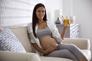 Obraz na płótnie Canvas Young pregnant woman with glass of juice in living room. Taking care of baby health