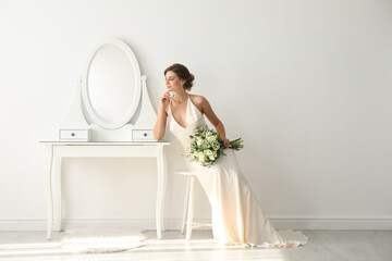 Young bride in wedding dress with beautiful bouquet near mirror indoors