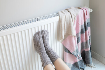 Woman is warm knitted woolen socks near a home heater in cold winter time. Using heater at home in...
